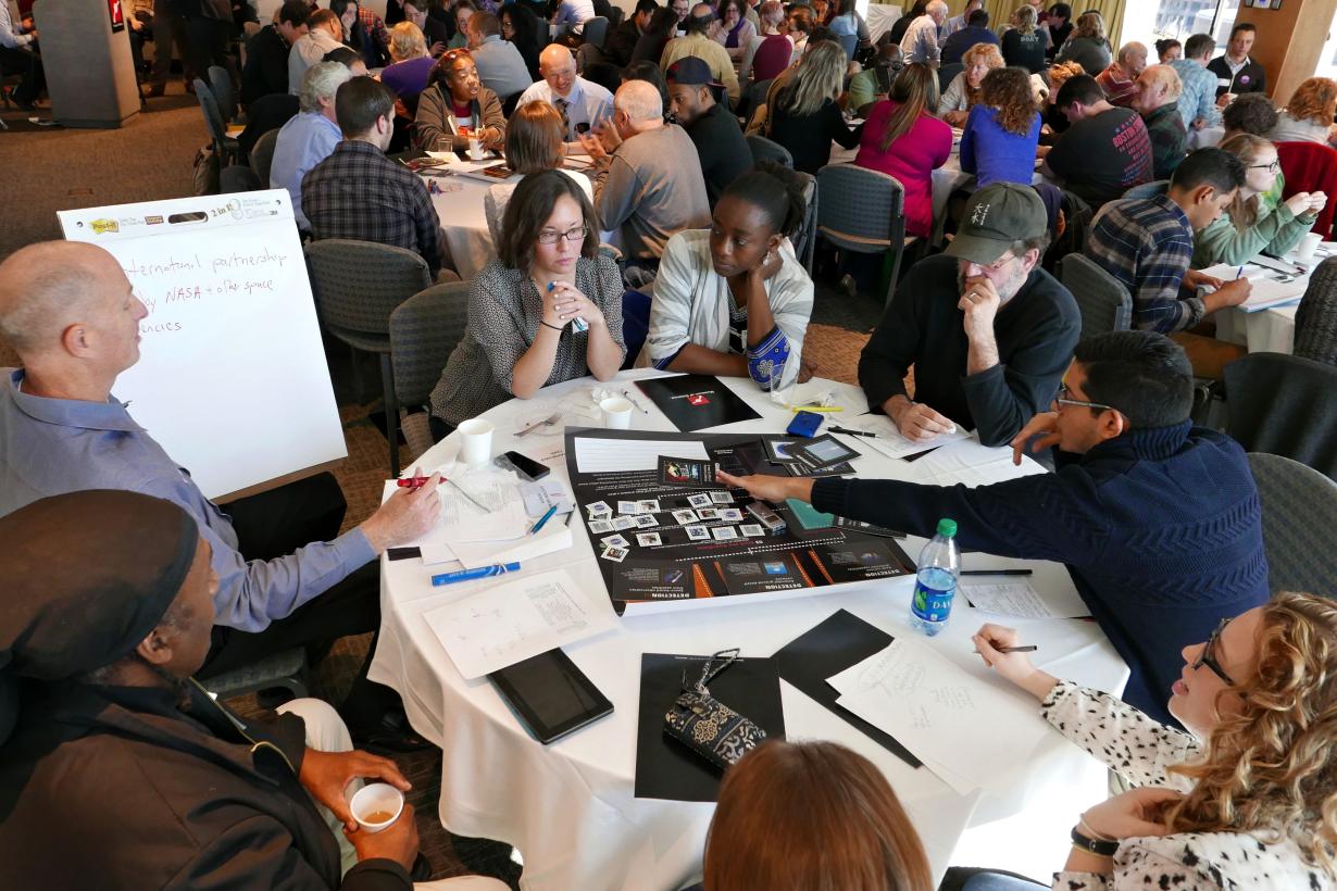 Museum of Science forums discussions featuring groups of people at tables writing on posters and discussing