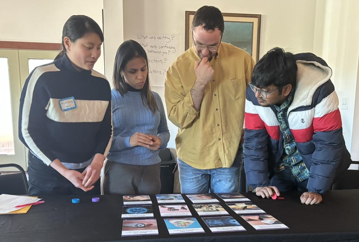 Crowd stands around a table where the Neuro Futures Card Game is Spread Across for Discussion