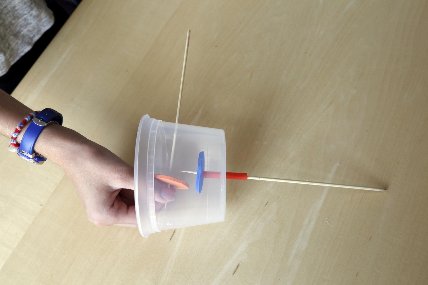 Automata inner mechanics - a hand holding the plastic container with two sticks and two oval foam pieces