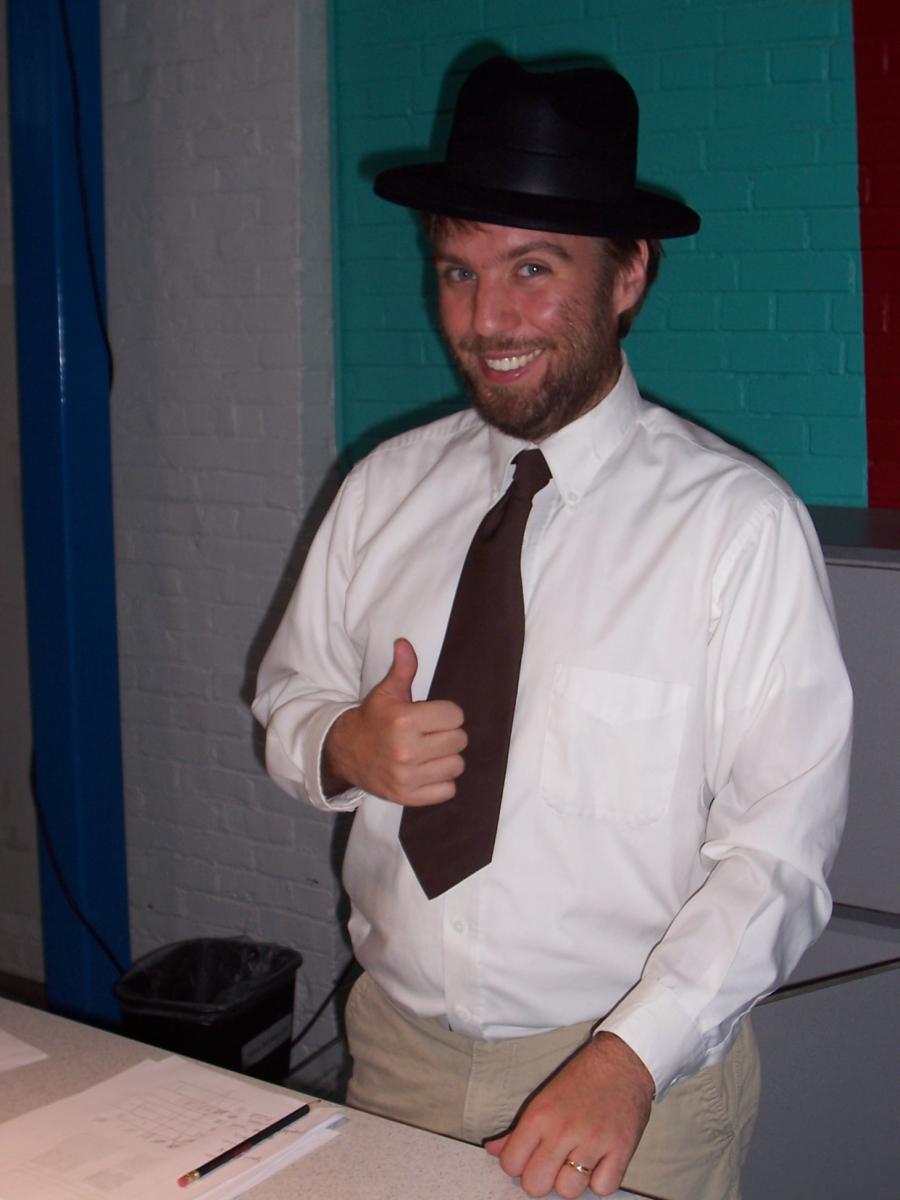 Facilitator in costume with a black hat and white button-down shirt playing a role in the story