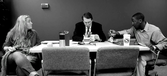 A black and white photo of three people sitting at a table having an intense discussion  