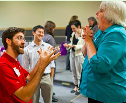 Man in red shirt and lady in blue shirt participate in a Improv exercise with other professional museum educators