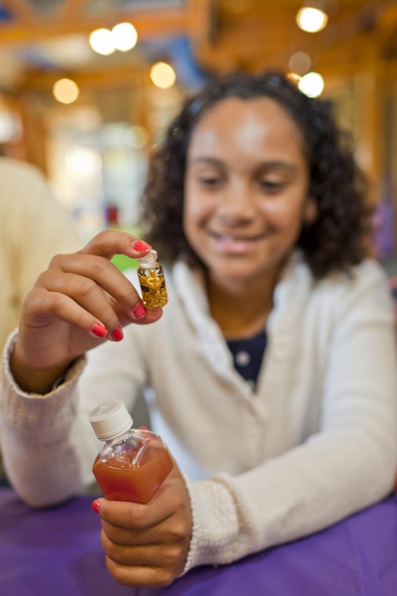 girl examining vial of gold flakes in NanoDays Nano Gold activity