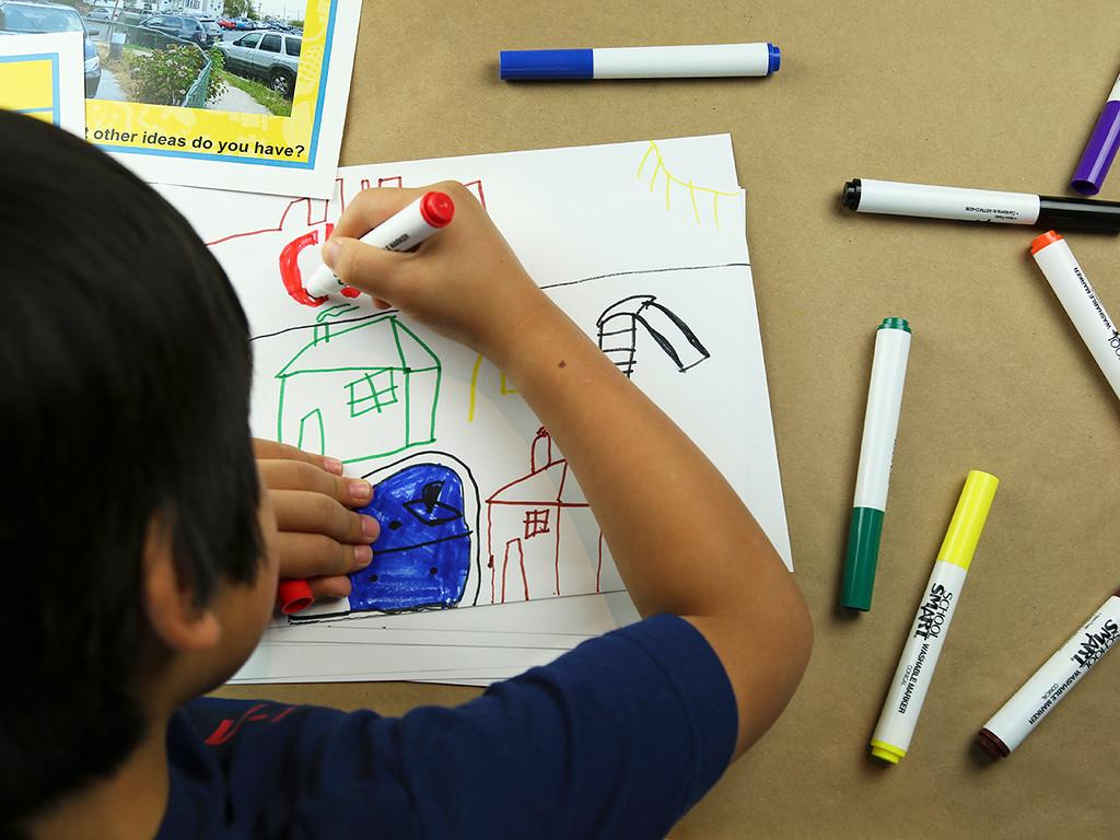 Child drawing a neighborhood with various colored markers