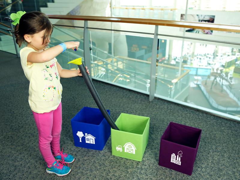 Child using tube to roll marbles into color sorted boxes