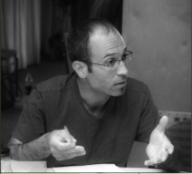 Black and white photo of a man in glasses discussing issues at a public forum