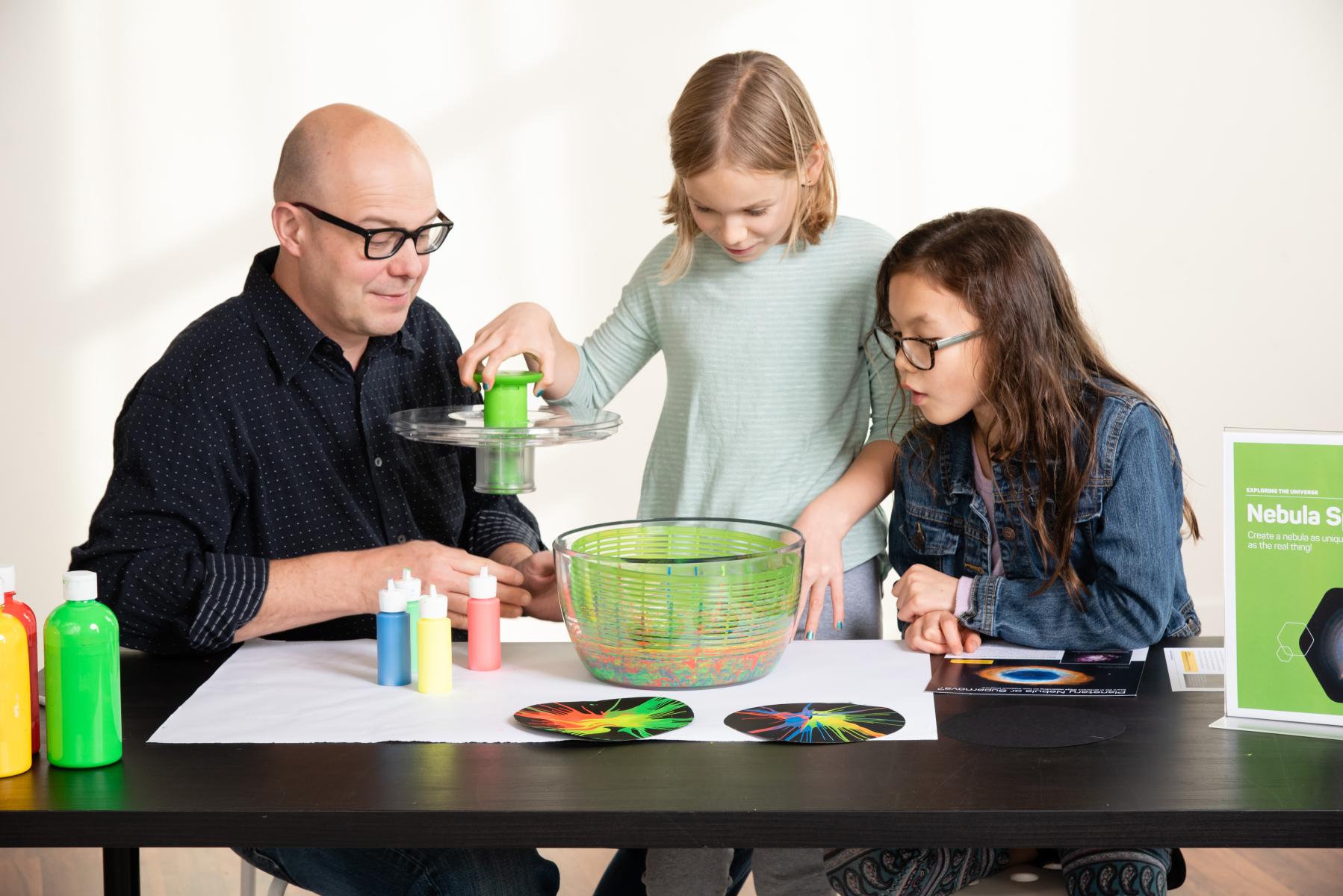Family of three load a paper with paint into a salad spinner to create a paint nebula