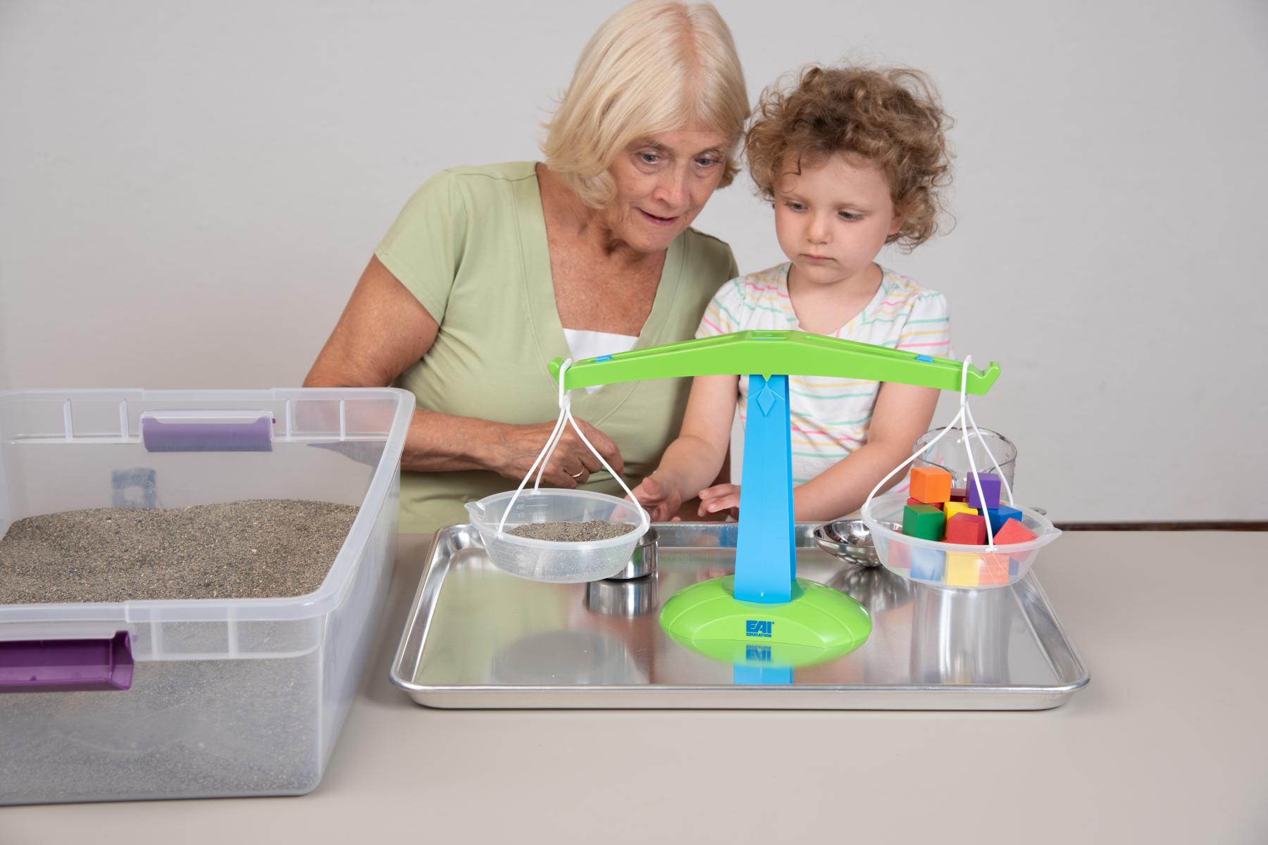 Facilitator and young learner balance sand and blocks on a scale