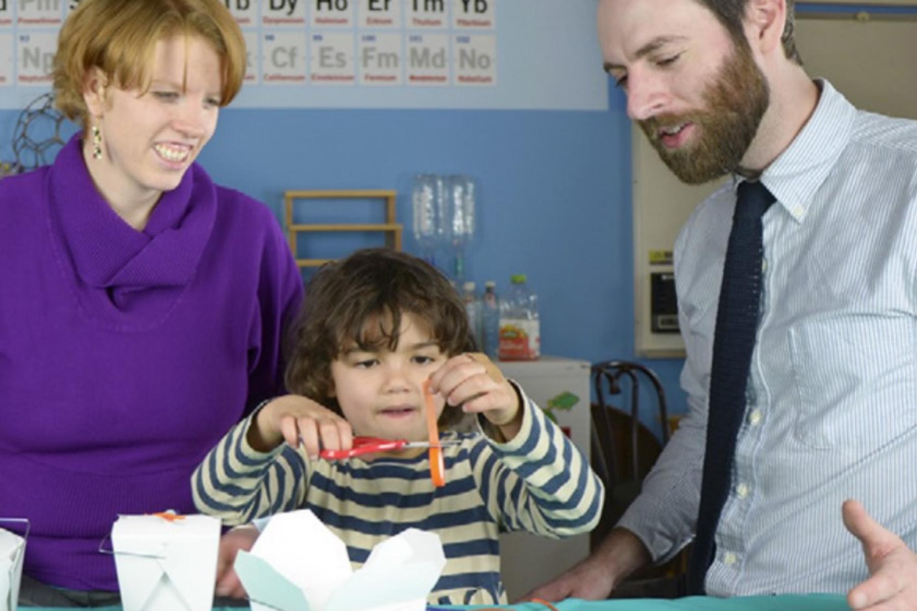 Mother and Facilitator watch as child cuts string for the VirEx Delivery activity