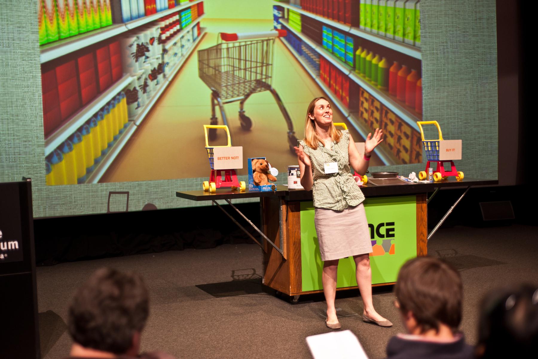 Presenter on stage with large powerpoint screen and props