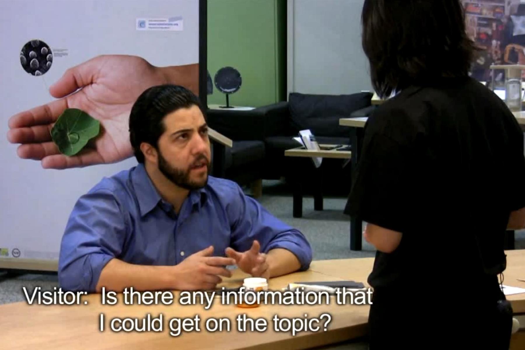 a bearded museum visitor asking a question to museum educator at a table