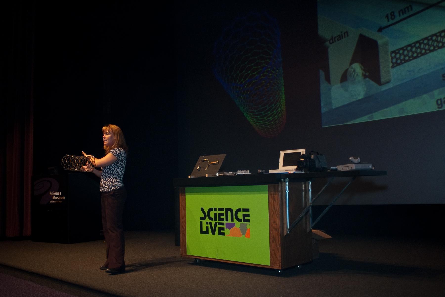 Presenter standing on stage holding a molecular model