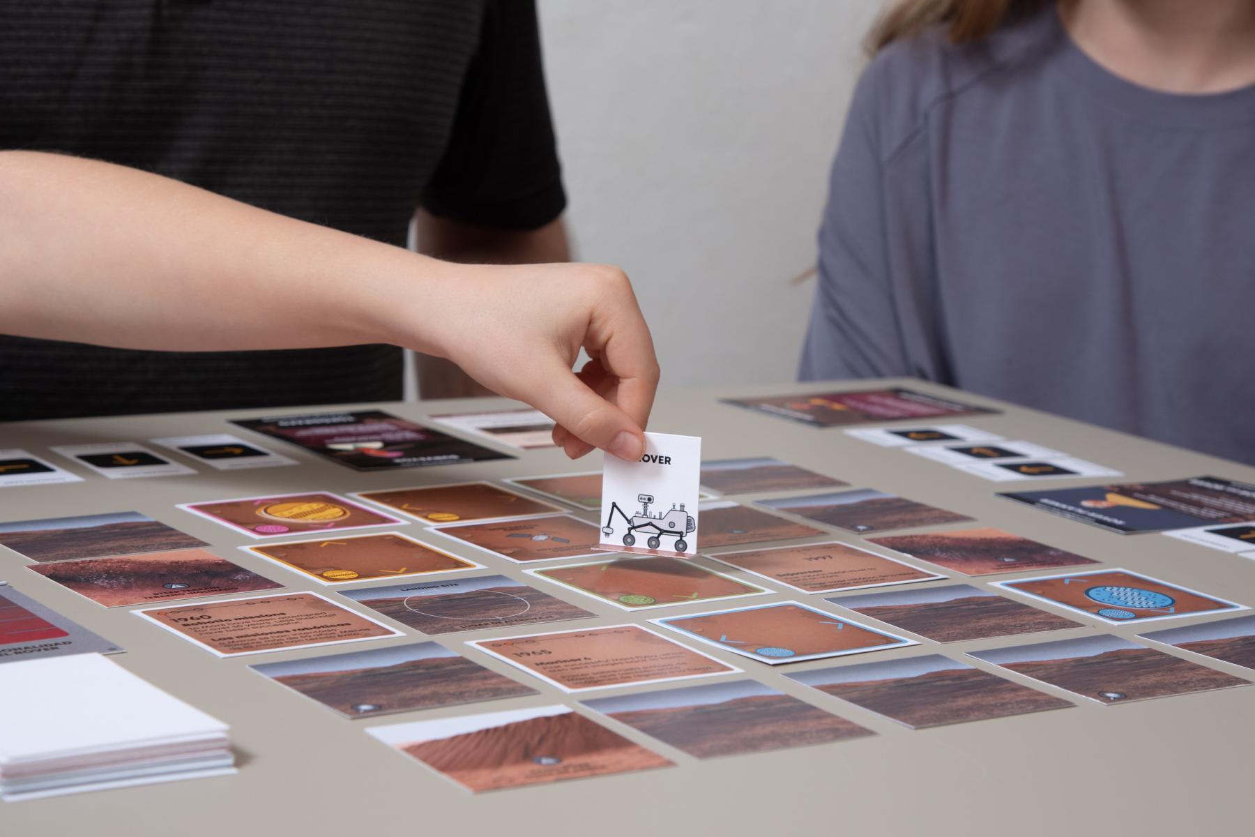 Hand holding Rover piece hovering over cards in Mars Rover board game