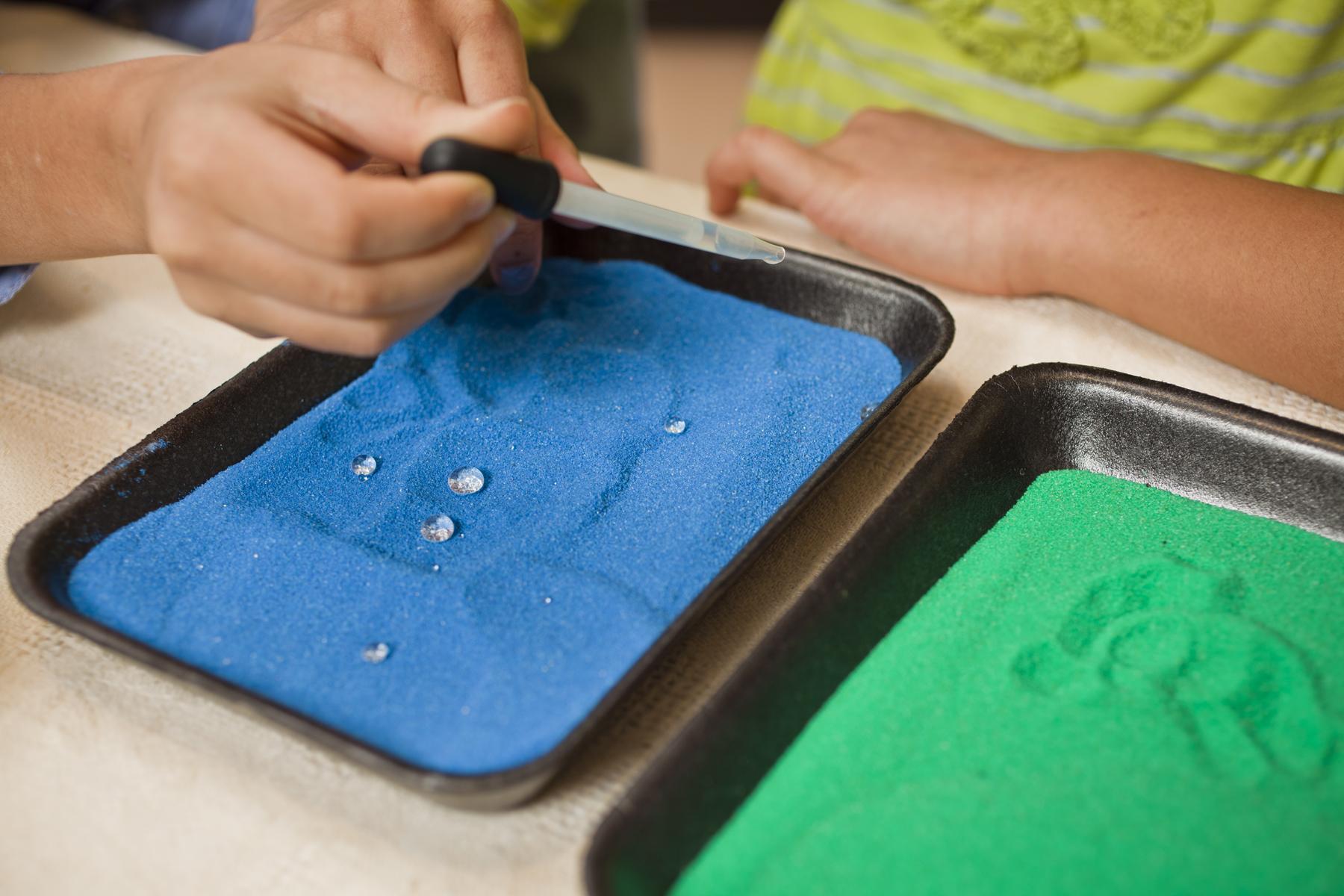 Two learners apply water droplets to hydrophobic sand wising a eyedropper 