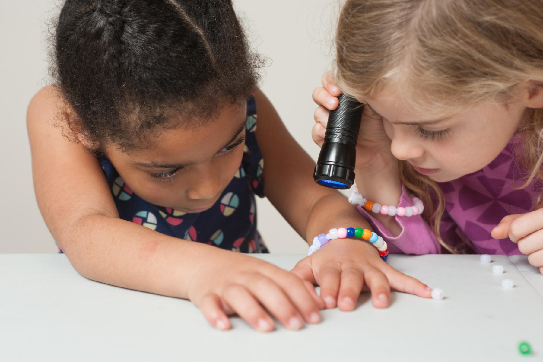 Two learners hold a black light to UV color changing beads