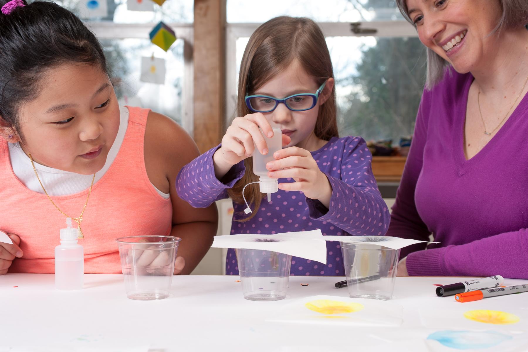 Two learners and a facilitator drip water onto a tissue to diffuse ink