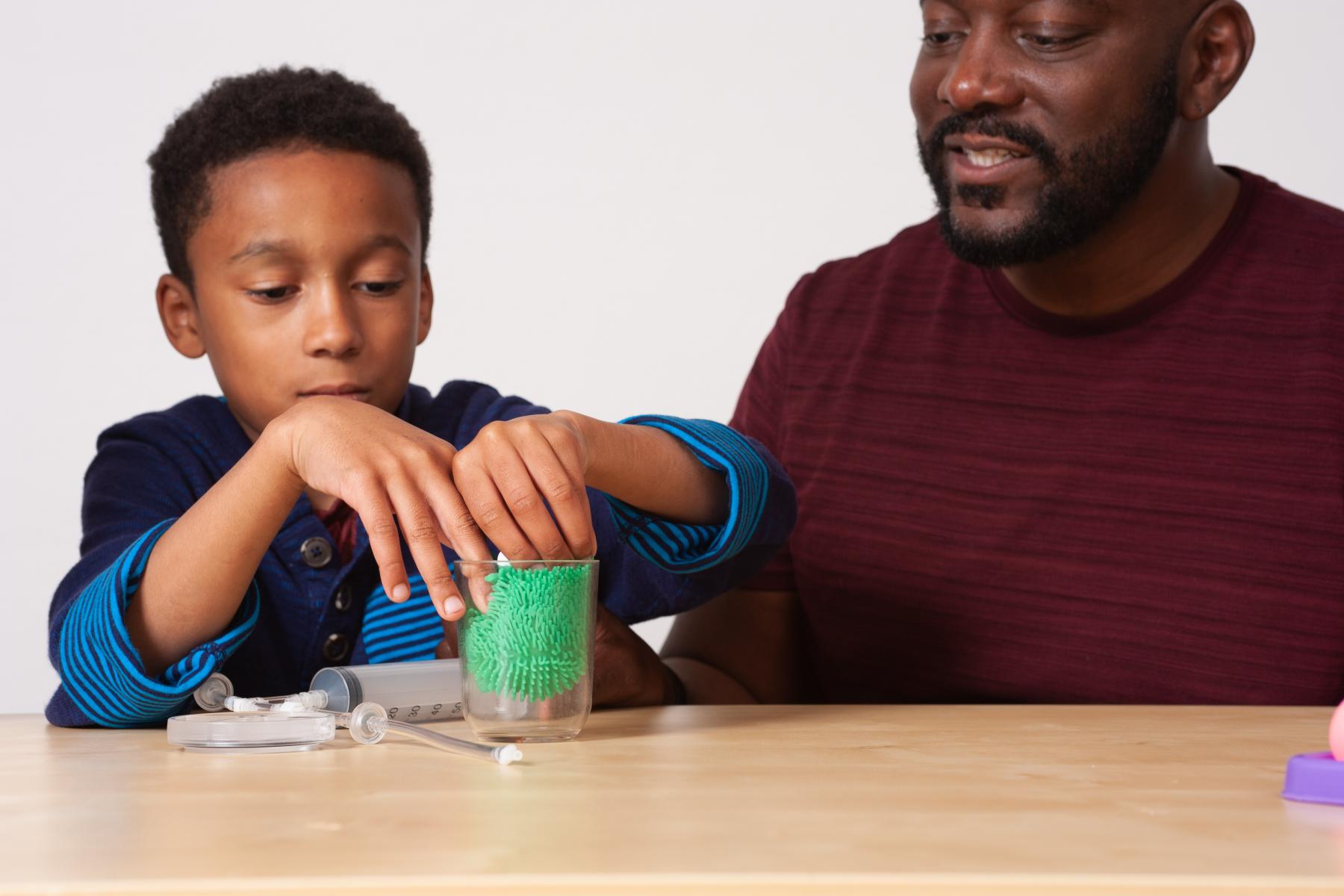 A young learner and a facilitator load a squish toy into a vacuum chamber