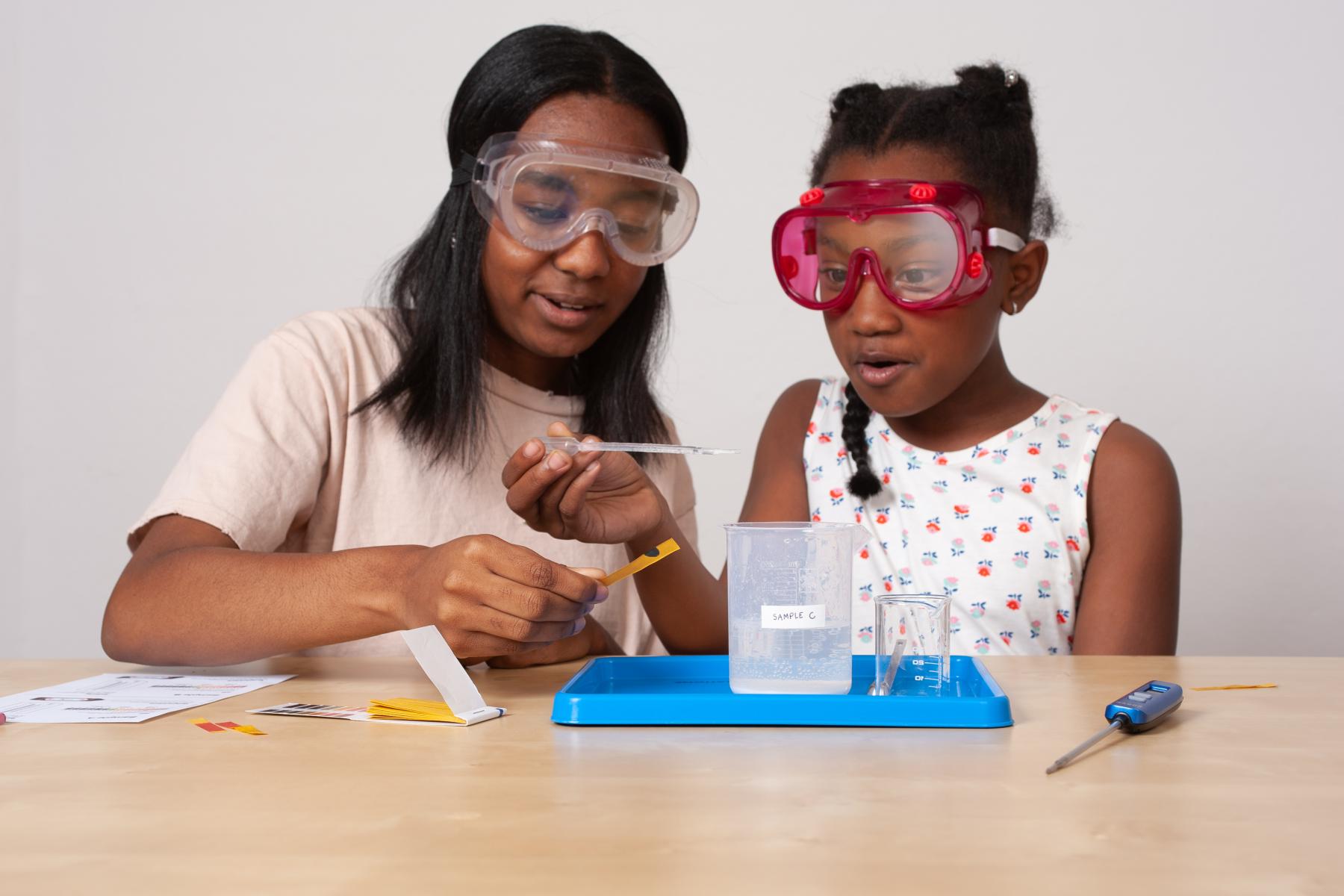 Two learners wearing goggles measure water pH with a pH indicator testing strip