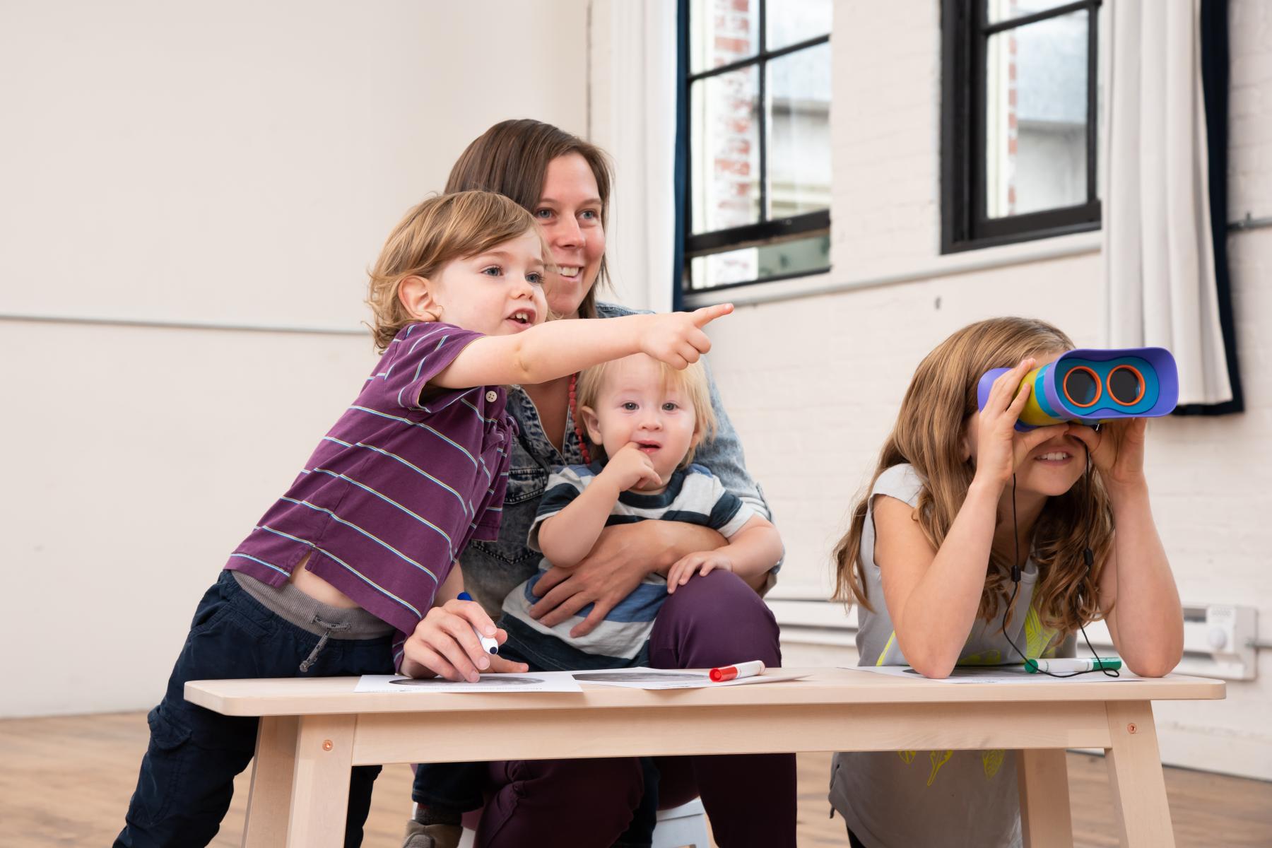 family with young learners use binoculars to look at a Moon poster