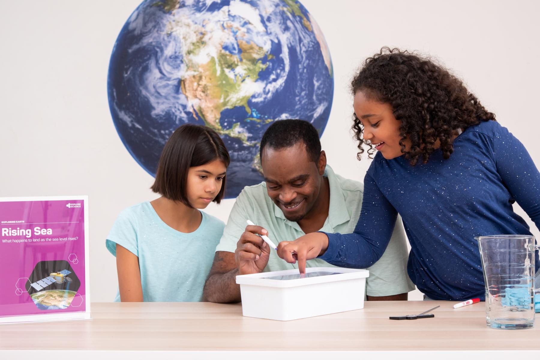 Family traces water line on clear piece of plastic in a model of a rising sea.