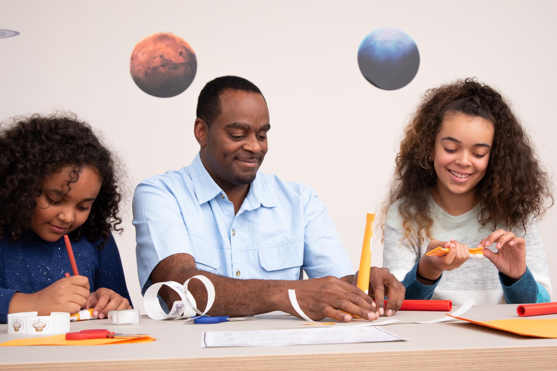 A family of three crafts their rockets out of paper, stickers and tape