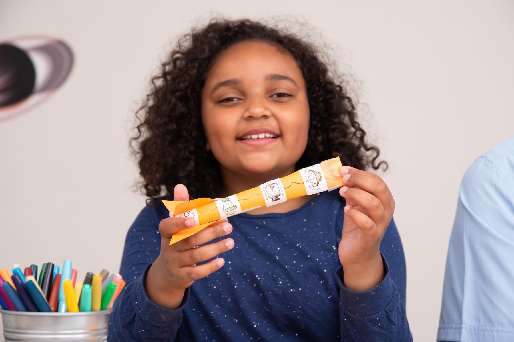 A learner shows the camera a paper rocket she made