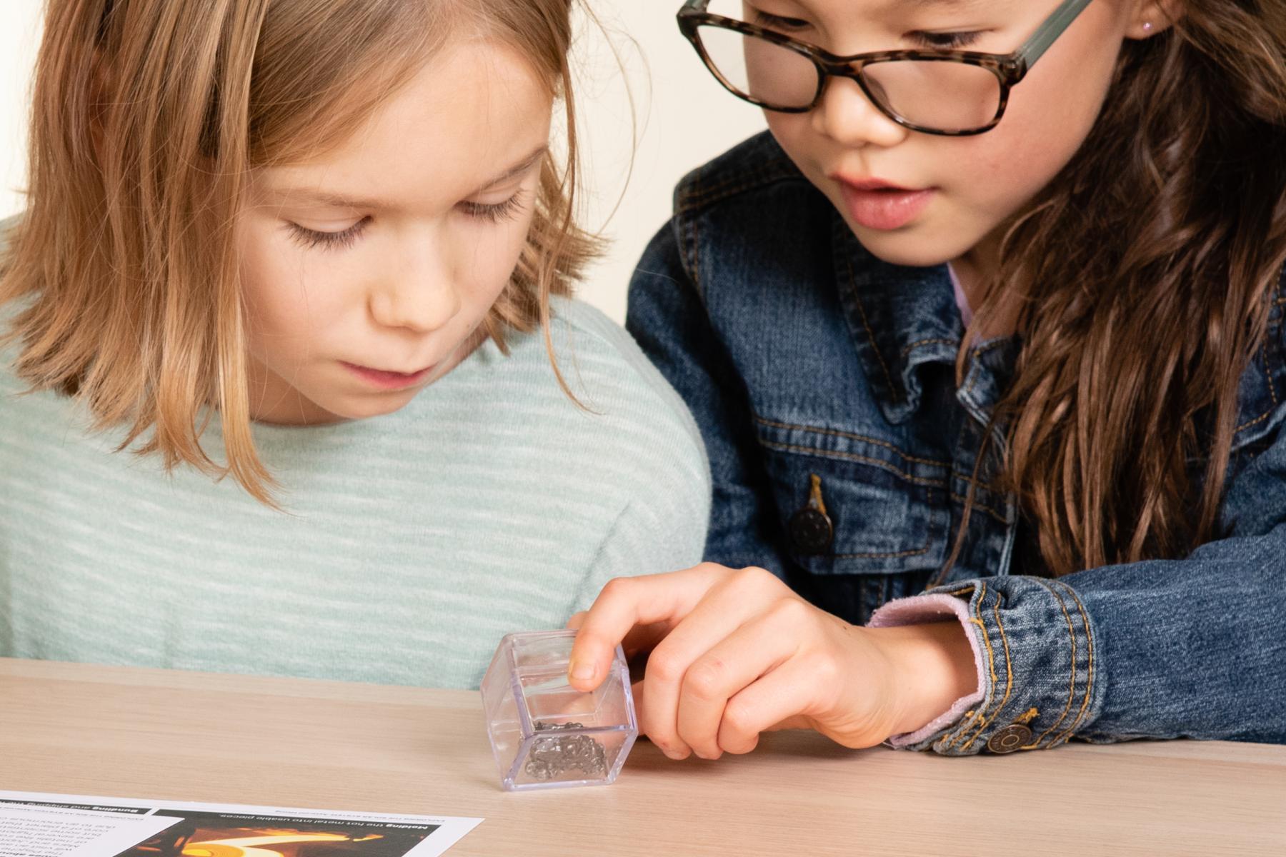 Two learners examine a sample of a meteorite under magnification box