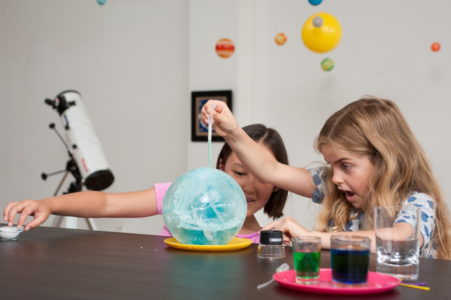 Two learners drip colored water onto a large sphere of ice