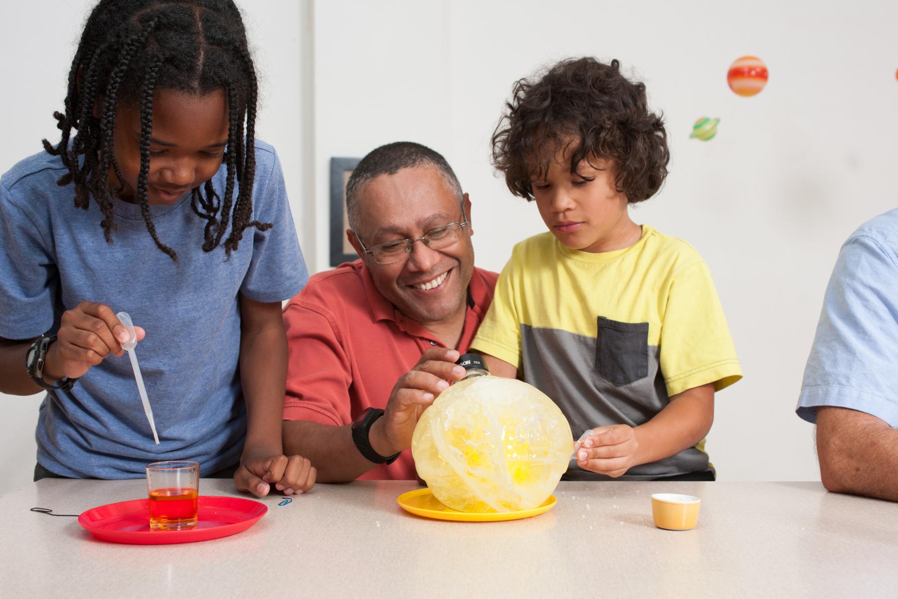 Two learners and a facilitator closely examine a large yellow sphere of ice