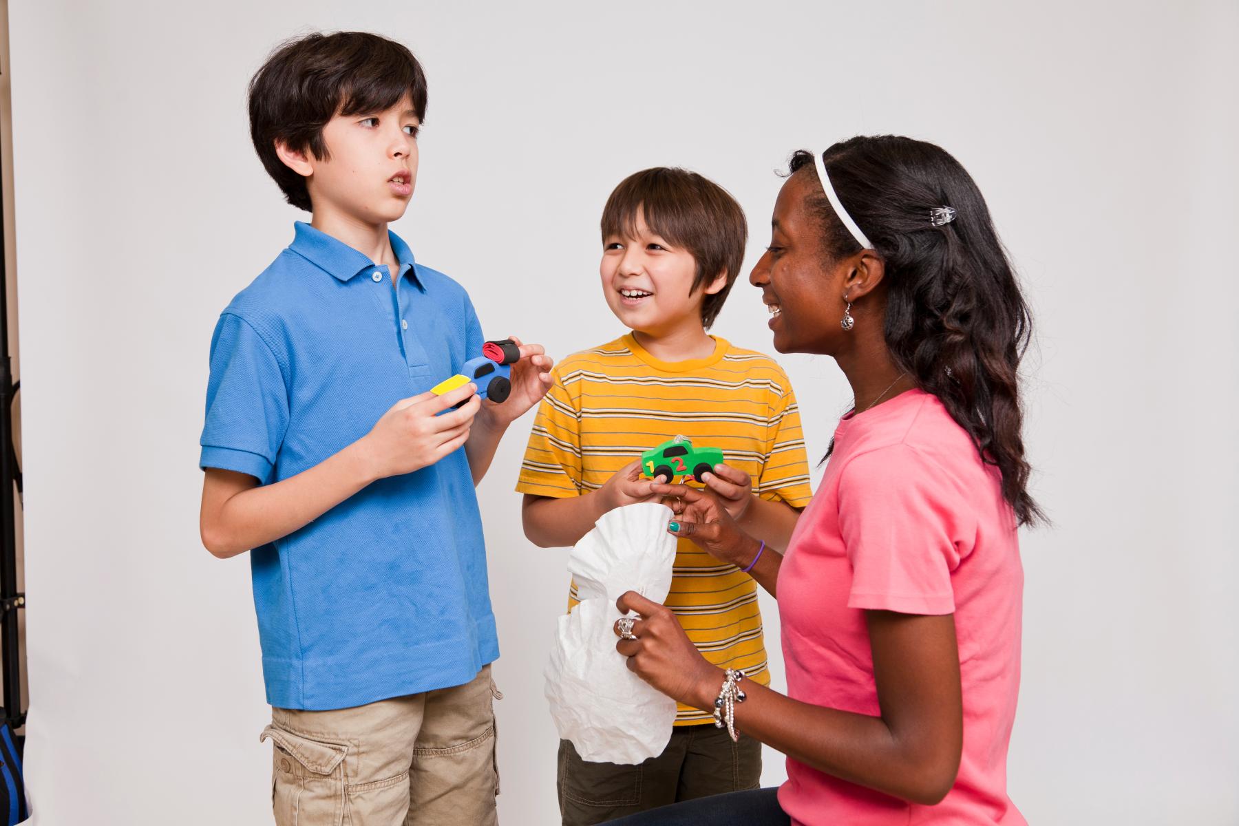 Two boys discuss their ideas for flying cars with toy car props to a facilitator