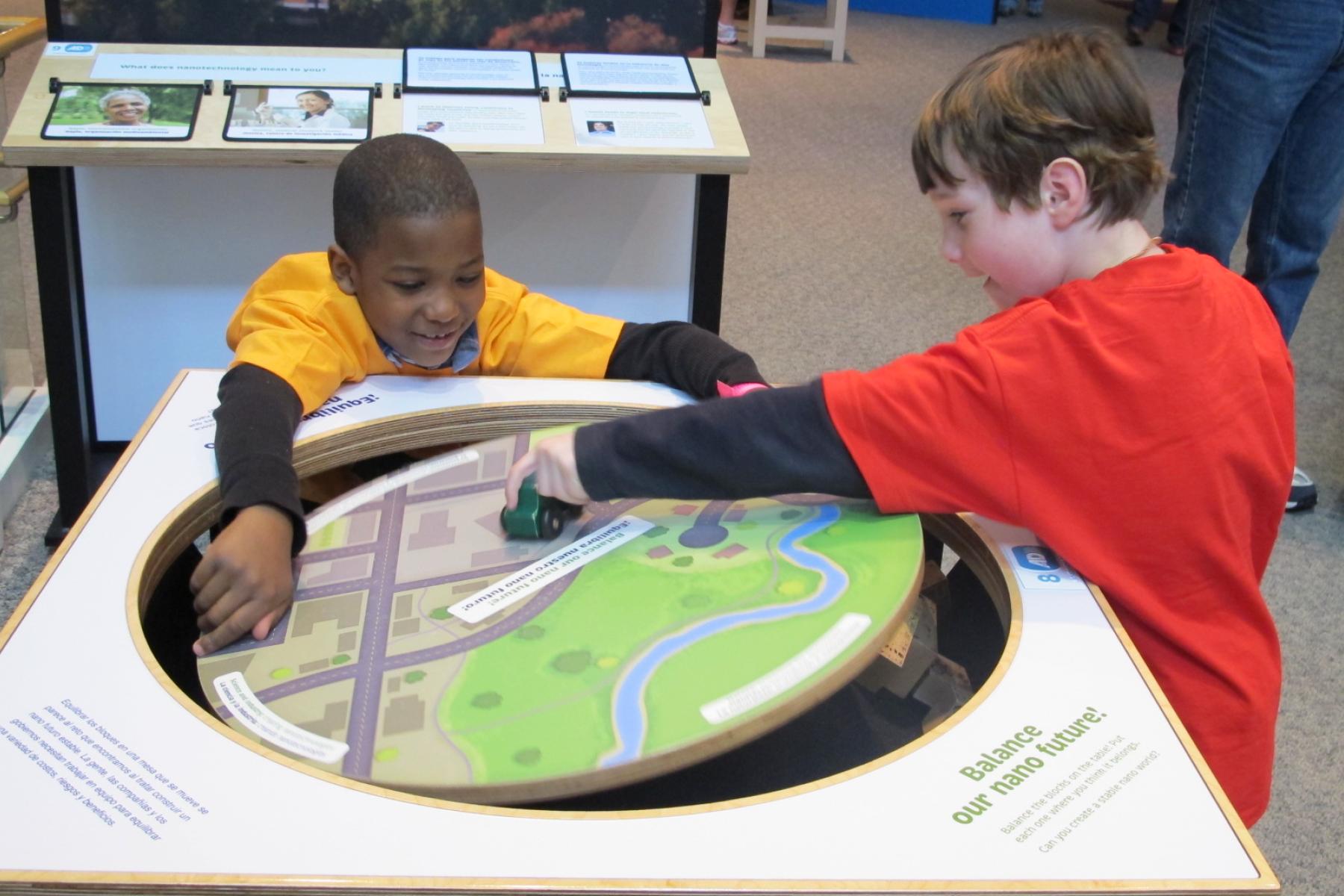 two boys play with the balance of the tippy table by setting different wooden blocks on its surface