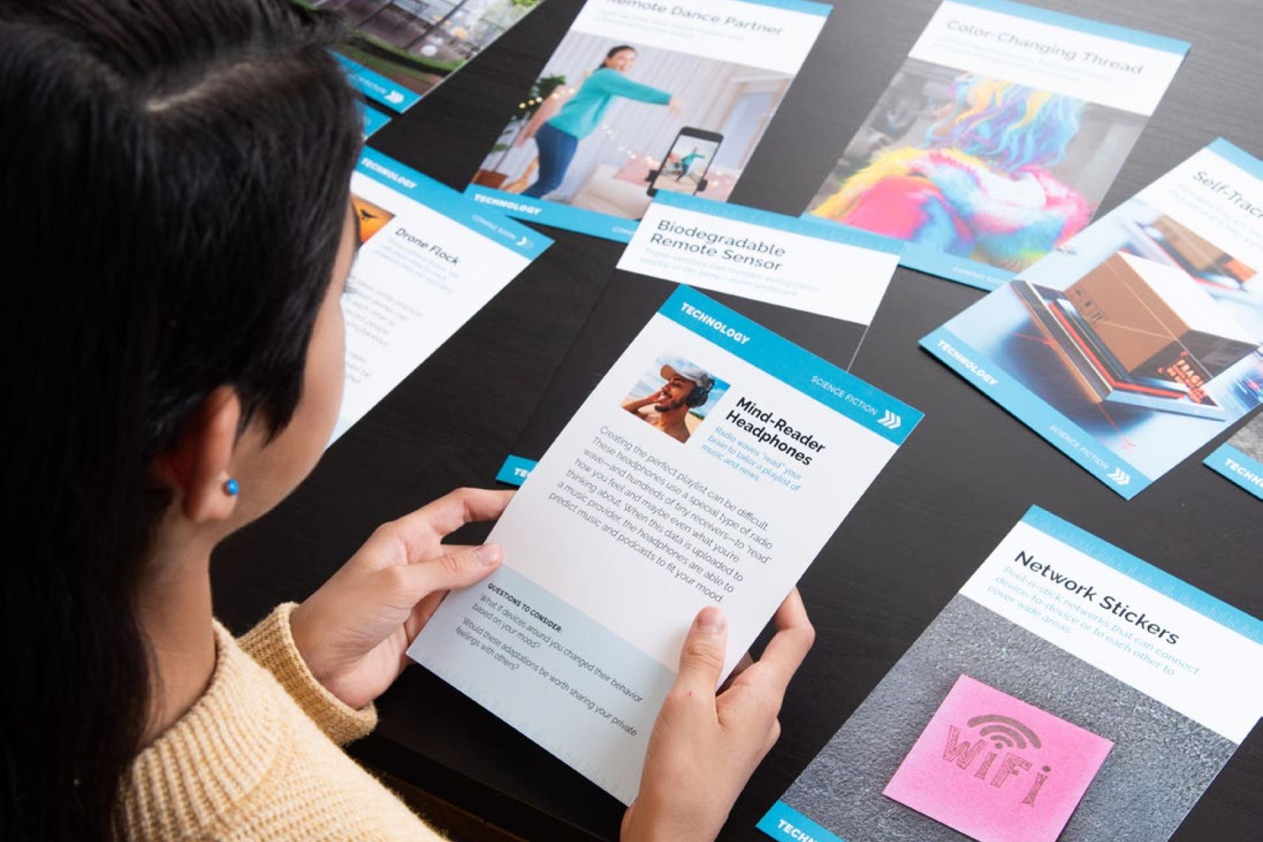 A view from over the shoulder of a child shows large cards that depict writing and various radio technologies spread across a table. The child is holding and reading one of the cards.