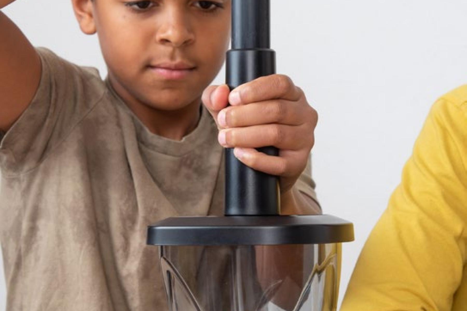 A child uses a hand pump to remove air from a vacuum-seal container that has an inflated balloon inside.