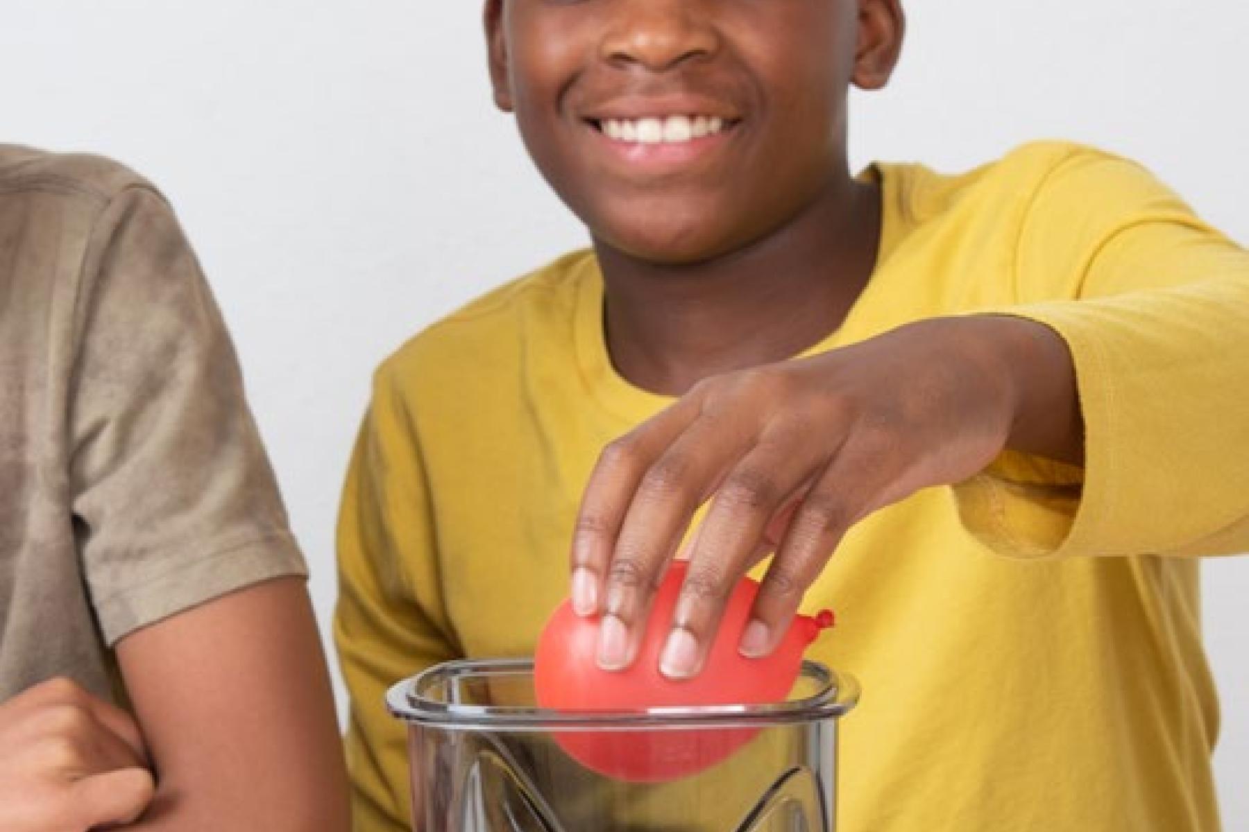 A child places a small, inflated balloon into a plastic vacuum-seal container. 