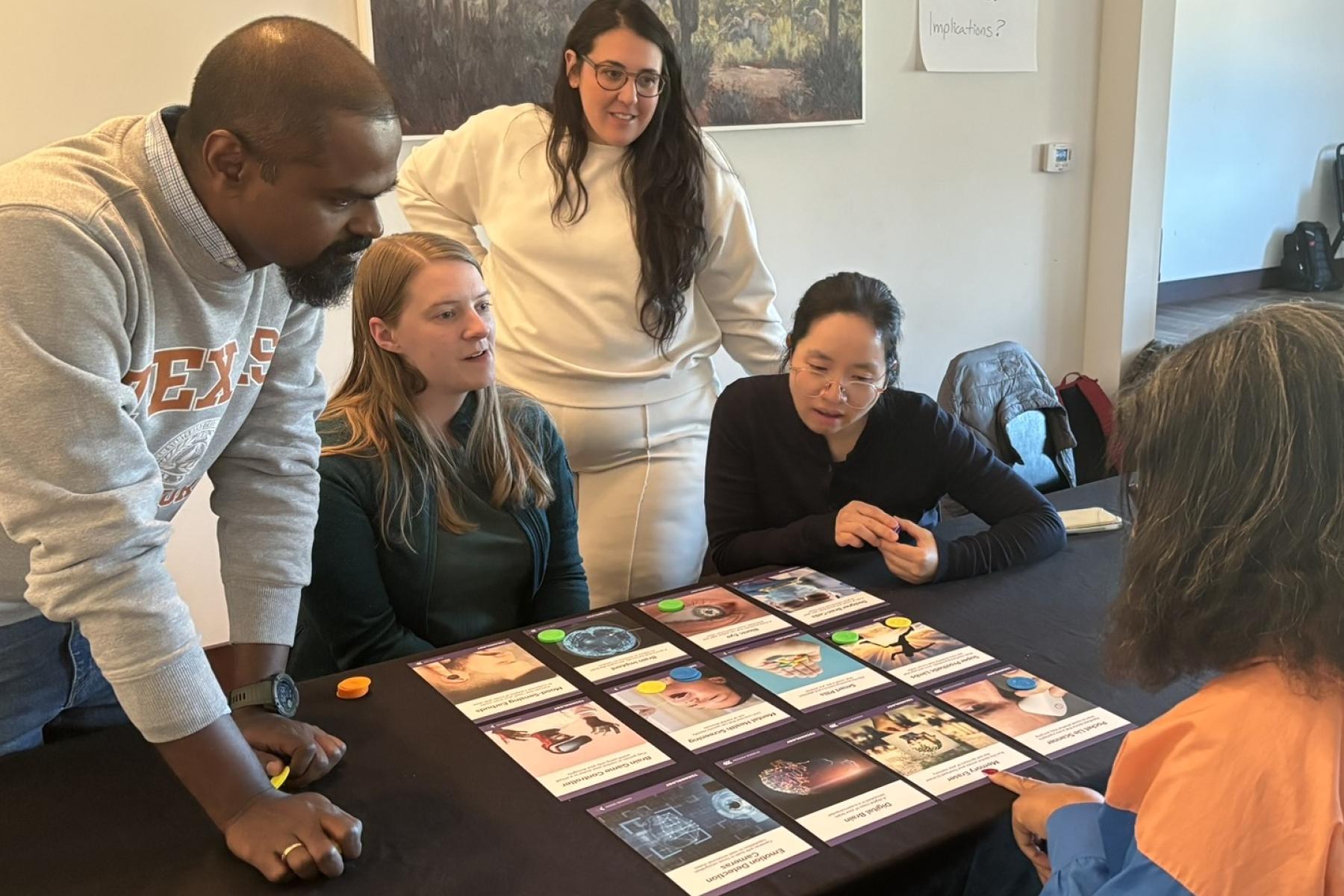 Crowd stands and sits around a table where the Neuro Futures Card Game is set out for Discussion