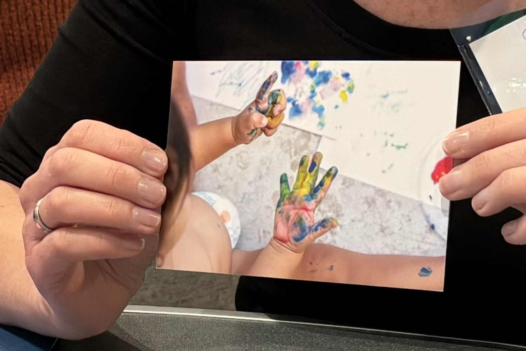 Hands holding up a What is Learning photo card showing toddler with paint