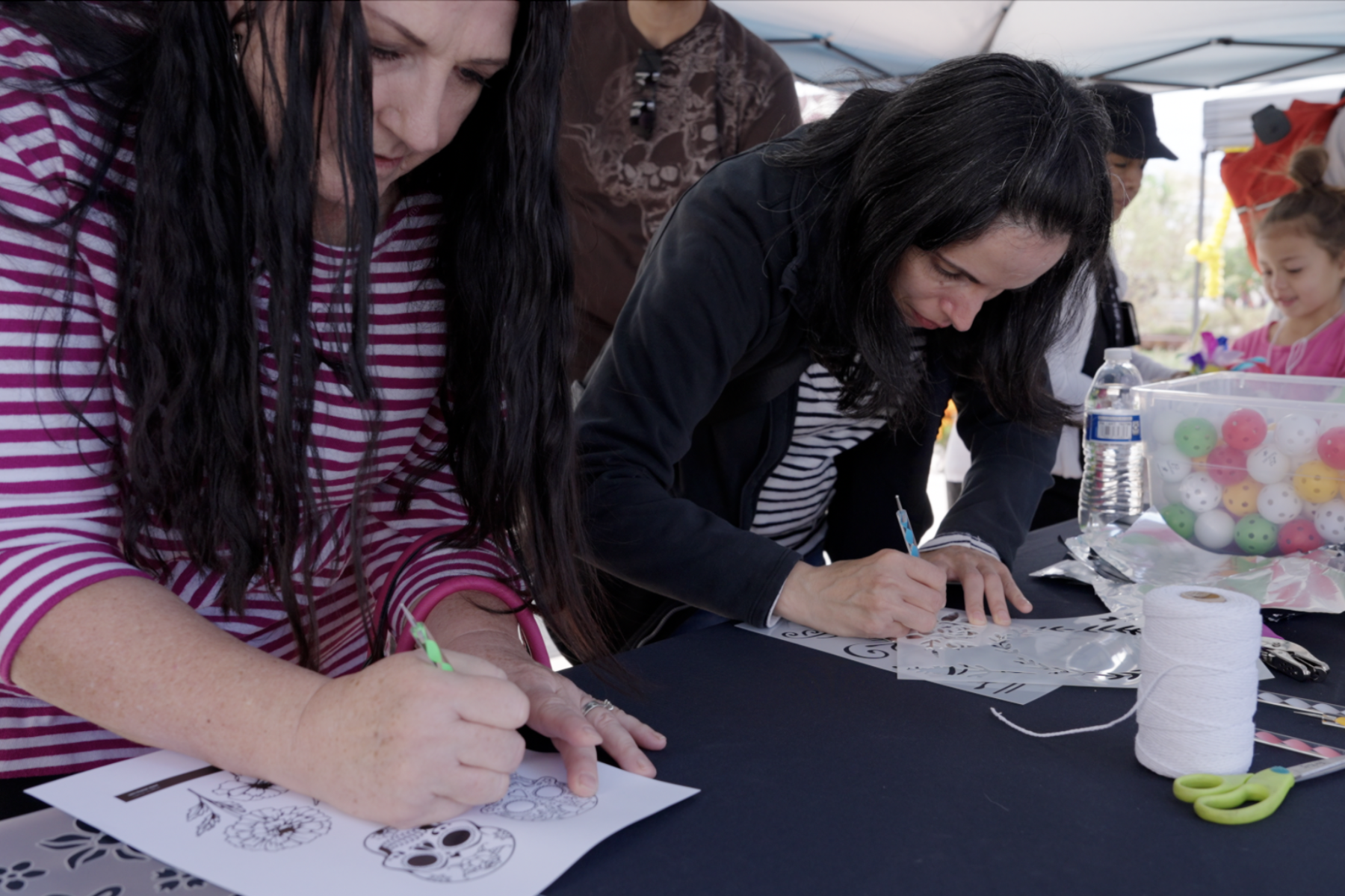 Two adults stand leaning over a table as they draw and trace onto foil.