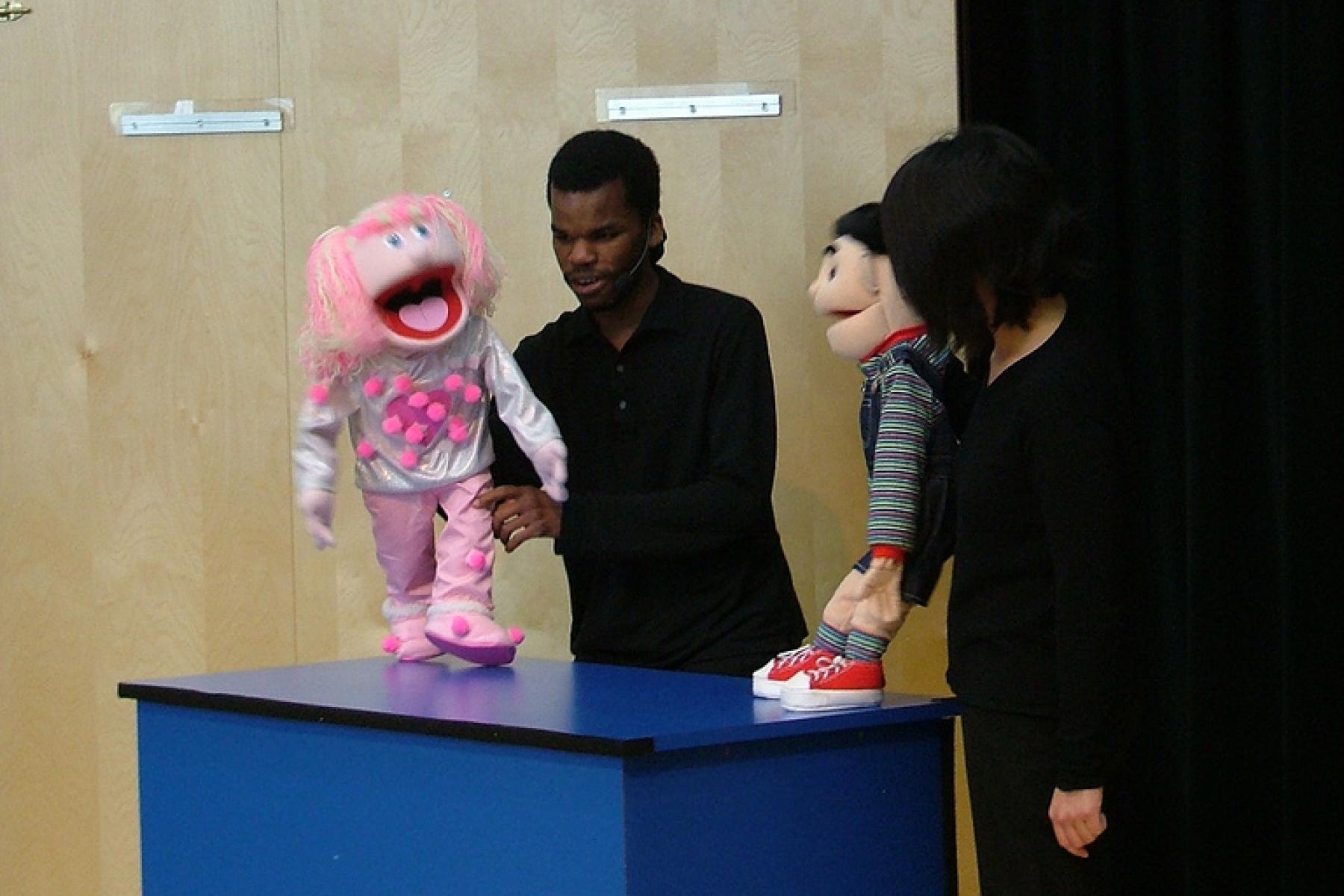two puppeteers on stage interacting with their puppets
