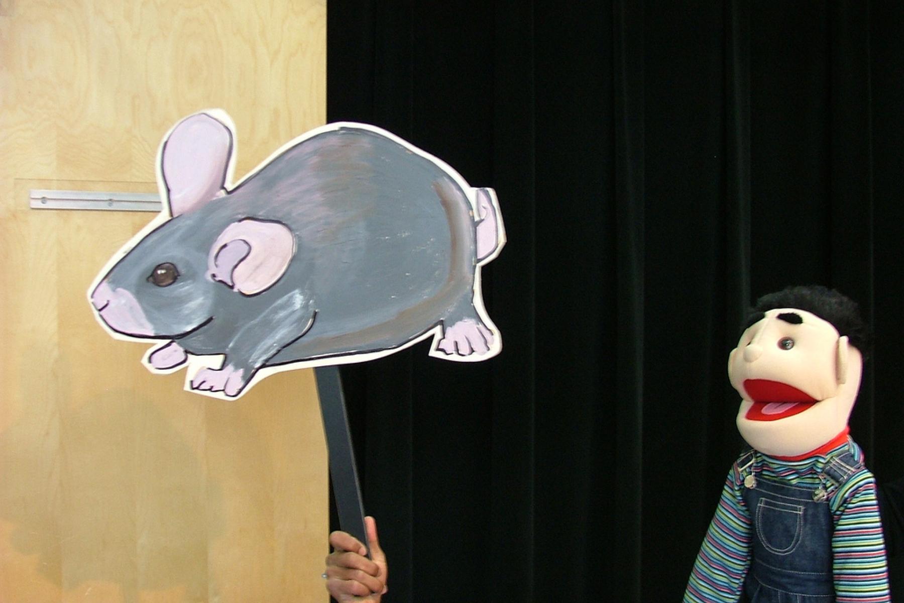 A puppet looking a picture of a mouse that has been placed on a stick.