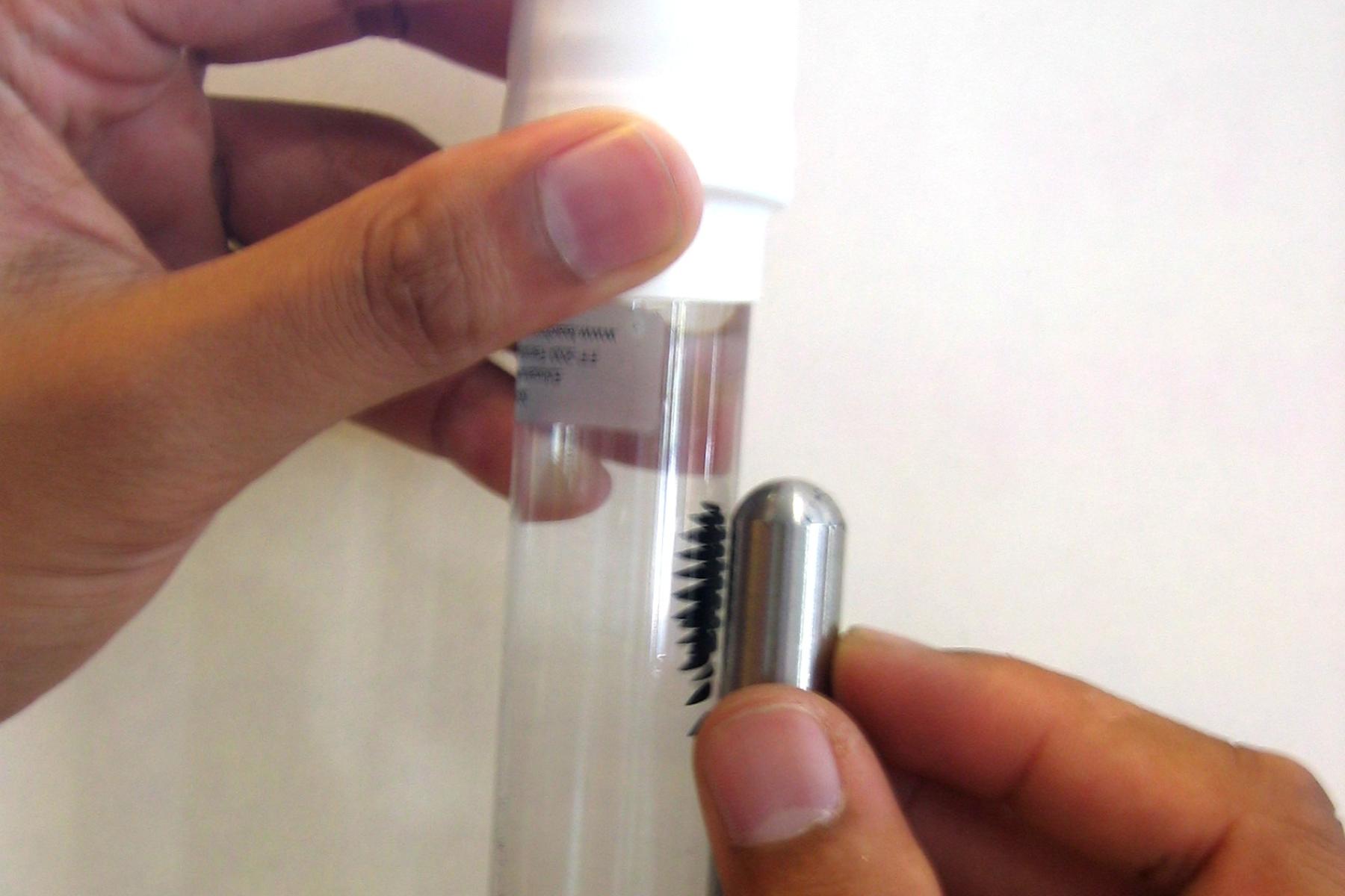 A tube of ferrofluid with a magnet held up to it and the ferrofluid is attracted to the magnet.