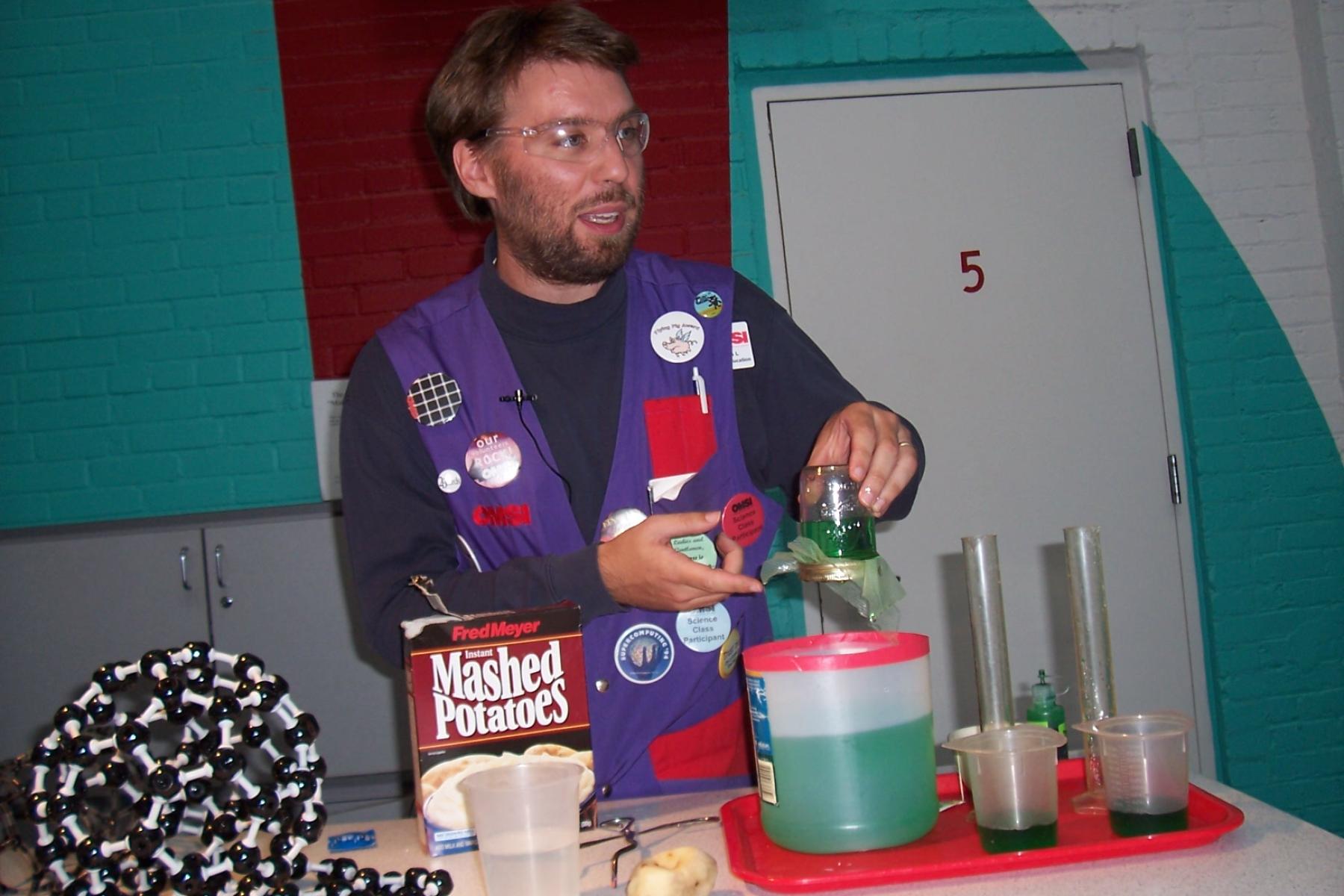 Faciltator showing physical models of carbon and liquids in jars on a cart