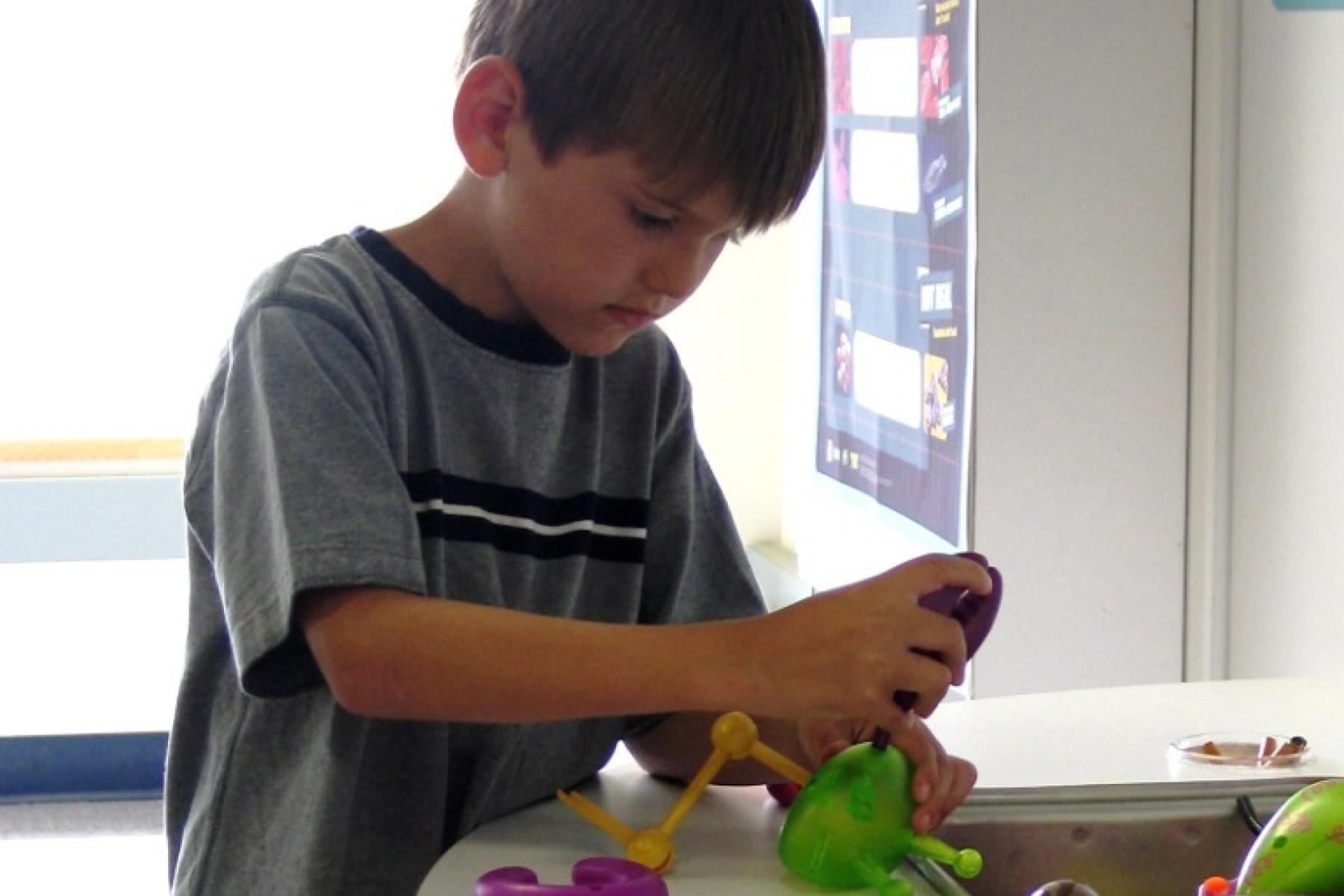 A young learner manipulating various colorful plastic objects in the Fact or Fiction? exhibit