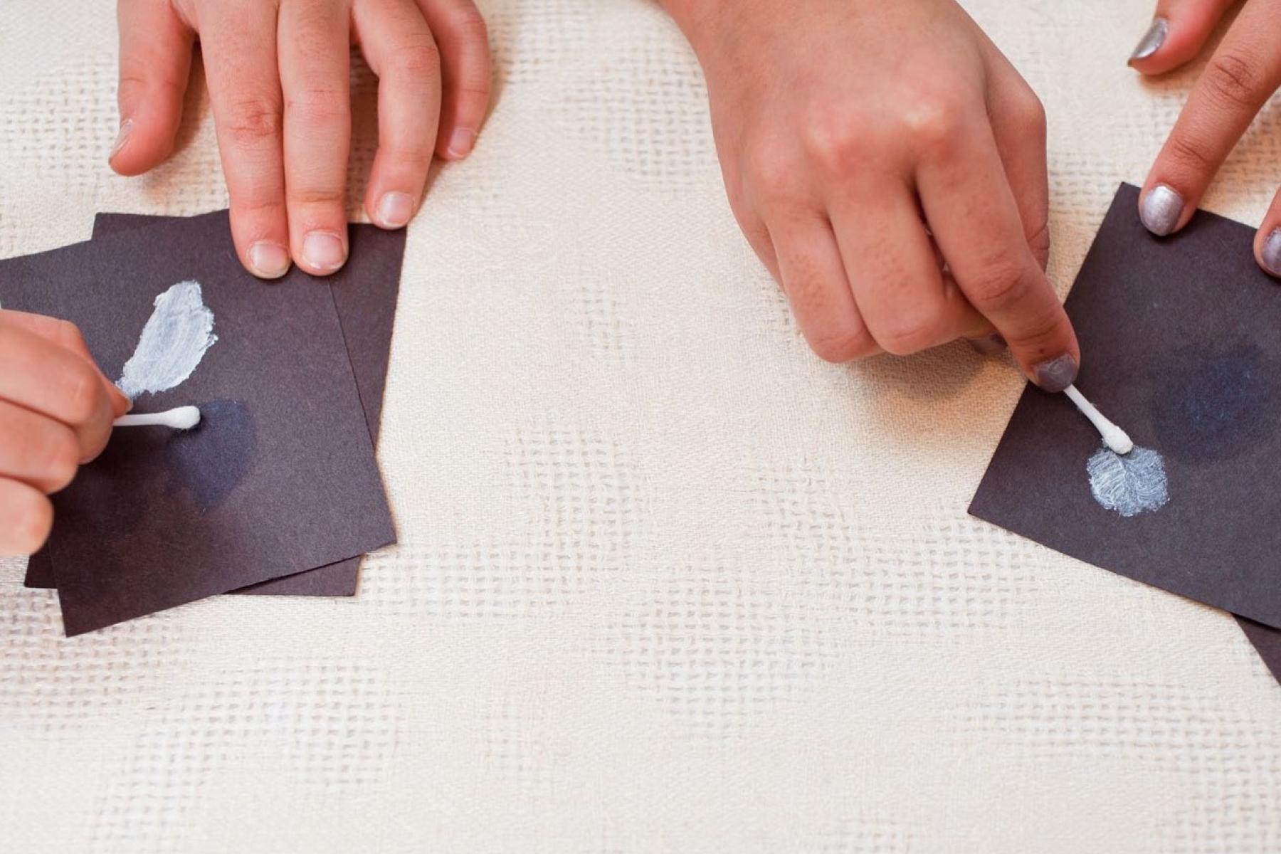 Hands using cotton swabs spreading sunblock on black paper using DIY Nano sunblock activity