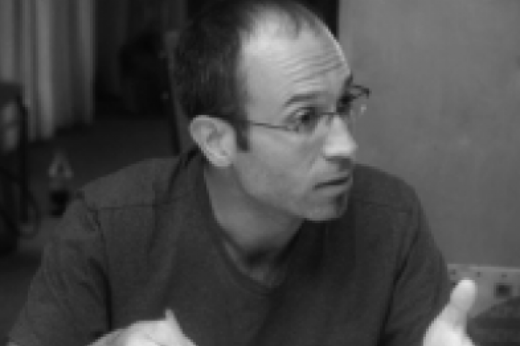 A black and white photo of a man with glasses intensely discussing a topic in a group