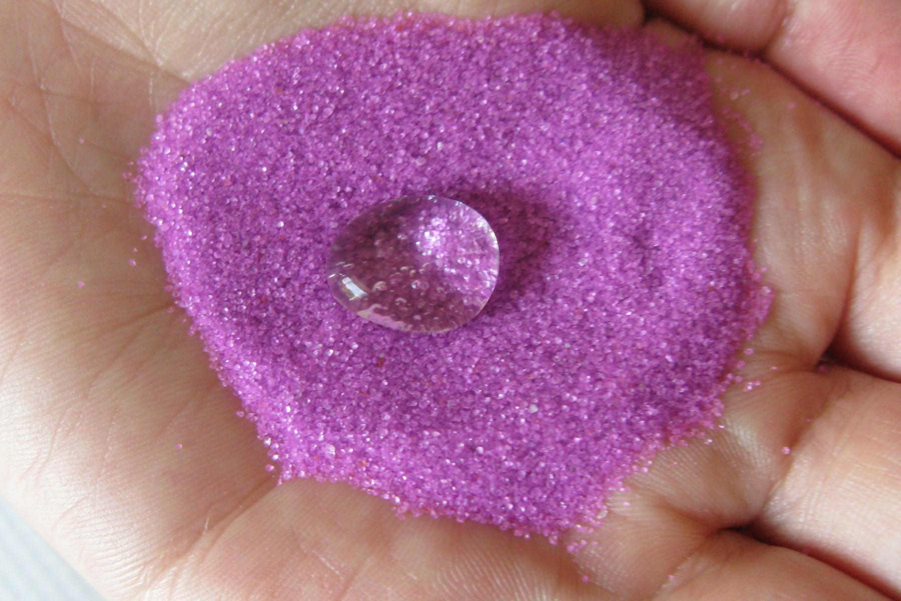 Exploring Products - Nano Sand's pink superhydrophobic sand.  A person is holding some pink sand with a big drop of water on top.