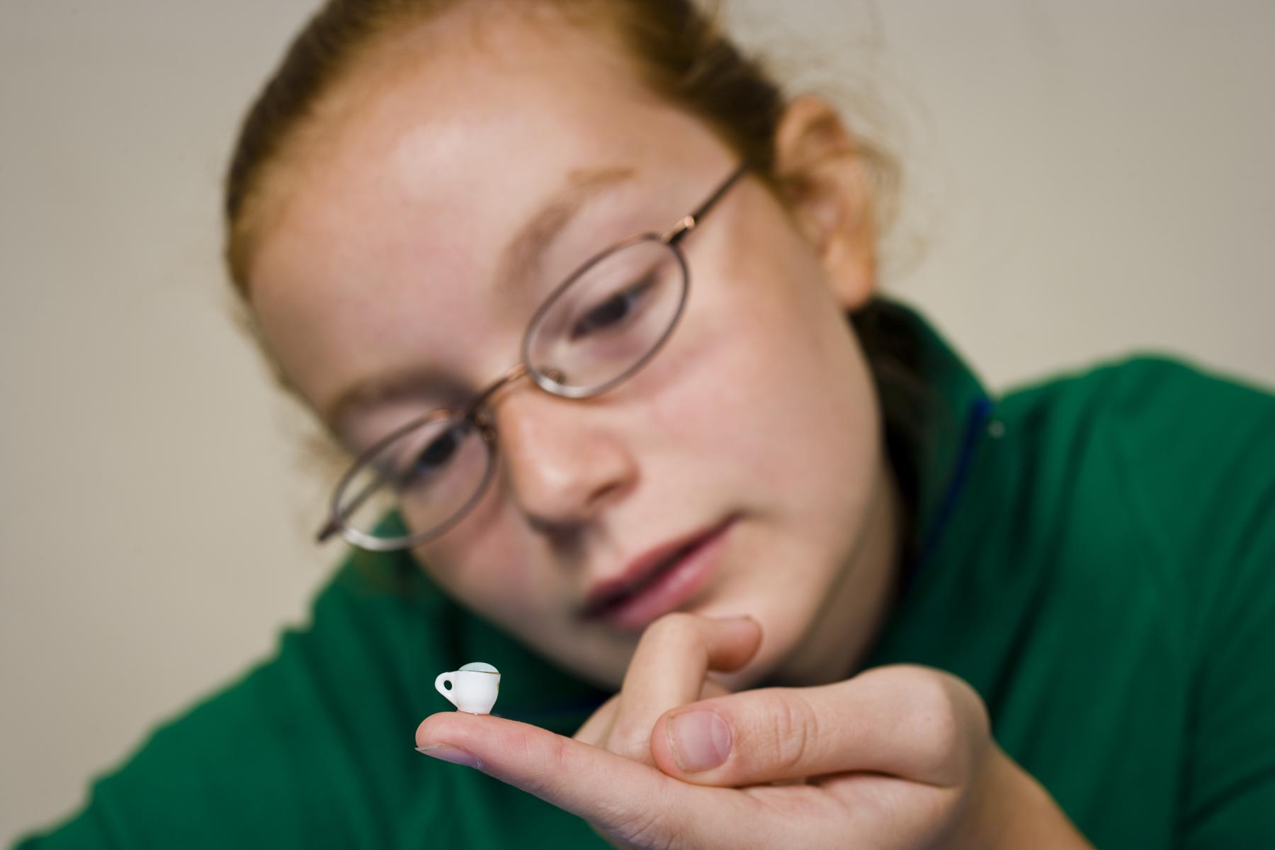 A person looking at a very very small teacup on the tip of their finger.