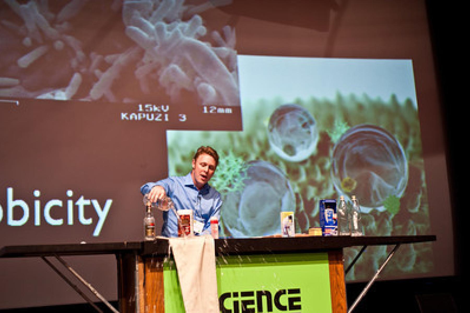 Educator on stage showing nano pants hydrophobic properties