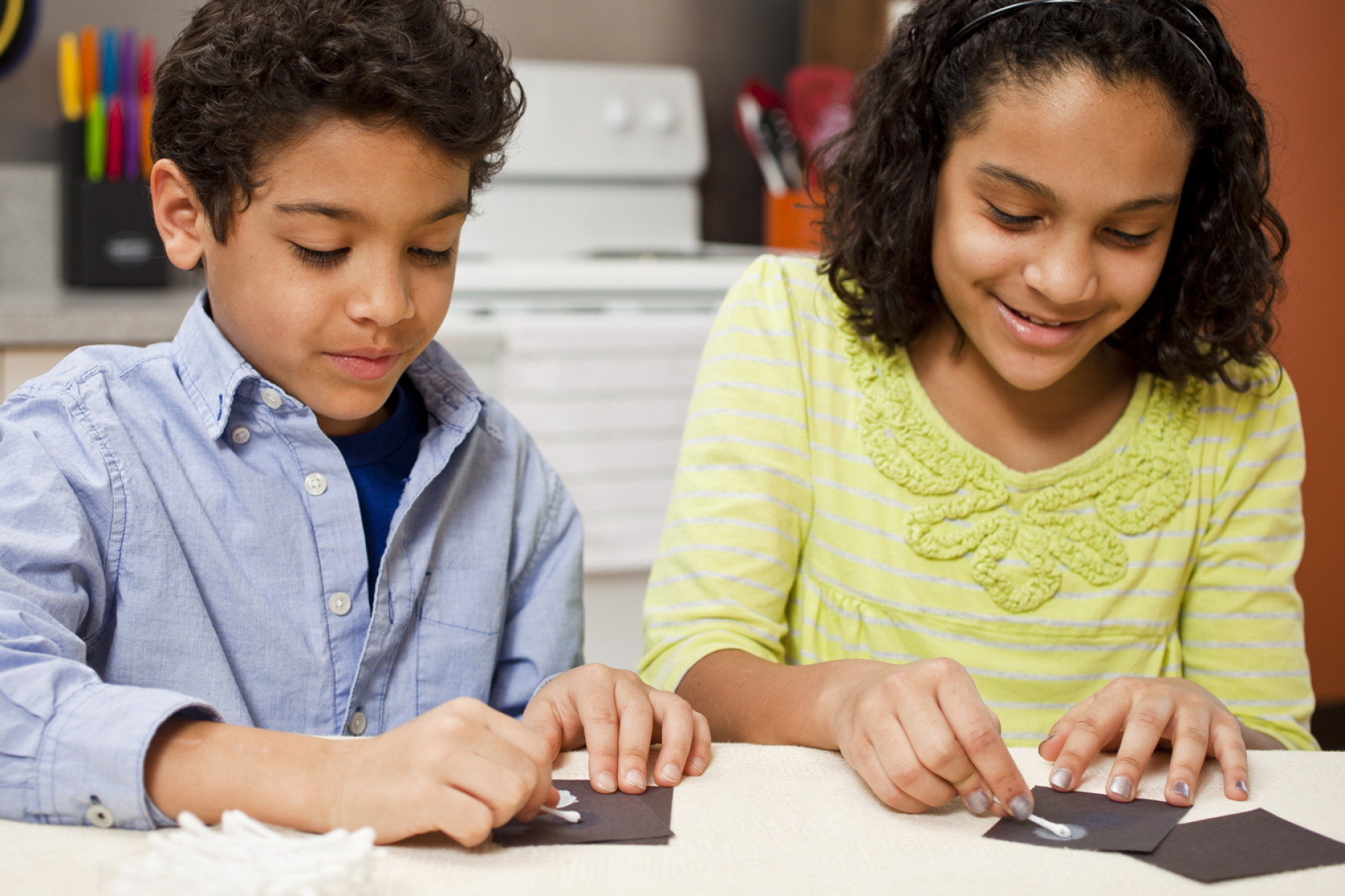 Two children applying sunblock onto a slip of black construction paper