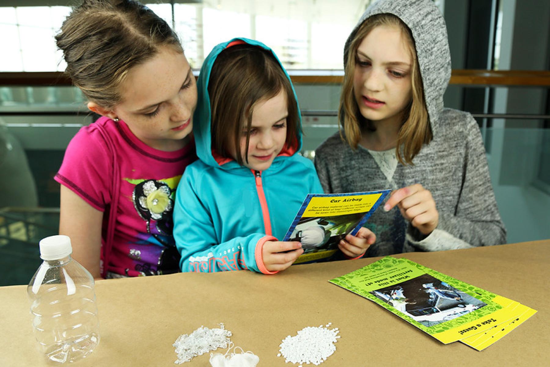 Image of three young learners looking at recycled materials card