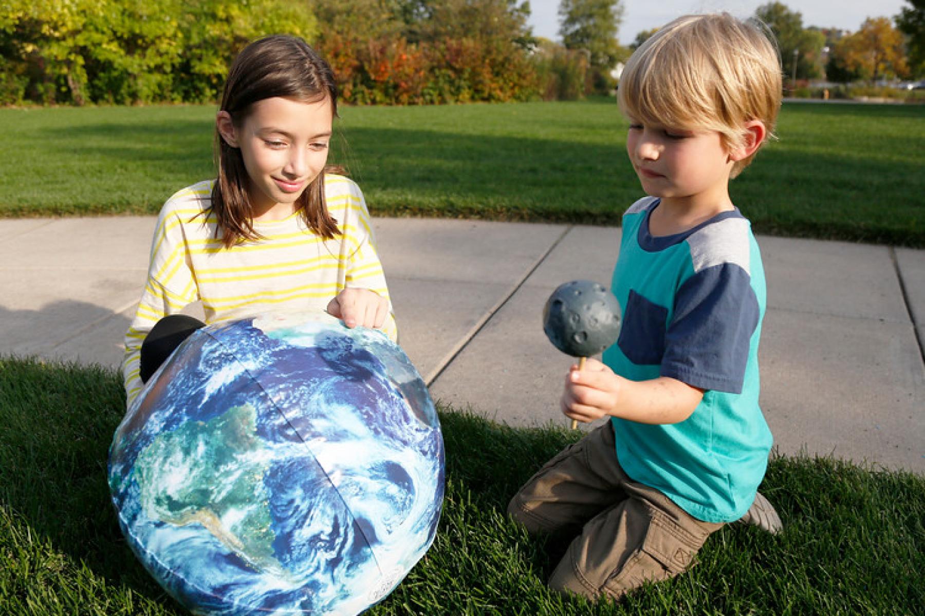 Two children using an inflatable Earth beach ball and a small Moon ball to compare the size of the Sun and the Moon and mimic an eclipse in the Exploring the Solar System: Solar Eclipse hands-on activity.